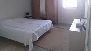 A simple, clean room with a bed, a small table, a wardrobe, and a window.