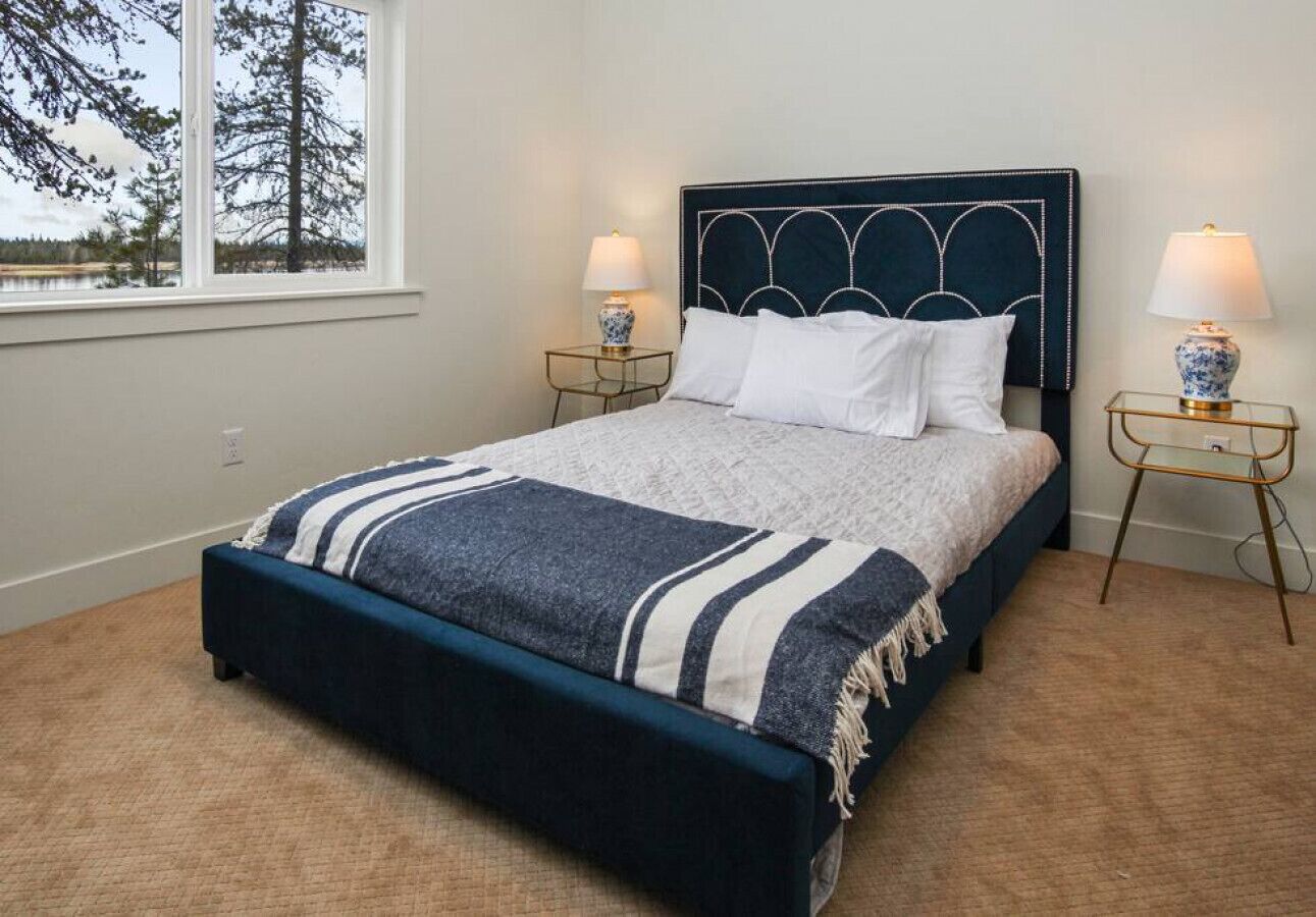 A bedroom with a dark blue bed, white pillows, a striped blanket, and two bedside tables with lamps.