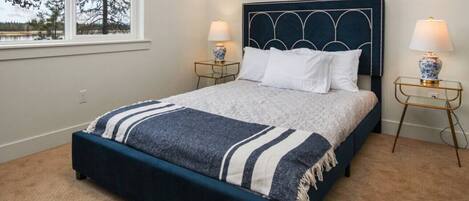 A bedroom with a dark blue bed, white pillows, a striped blanket, and two bedside tables with lamps.