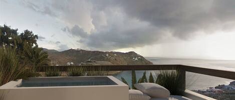 A modern outdoor seating area with a pool, overlooking a coastal landscape with hills and a view of the sea.