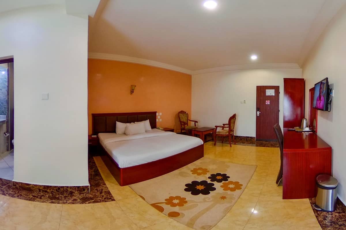 A hotel room with a bed, a desk, a TV, and a bathroom visible through an open door.
