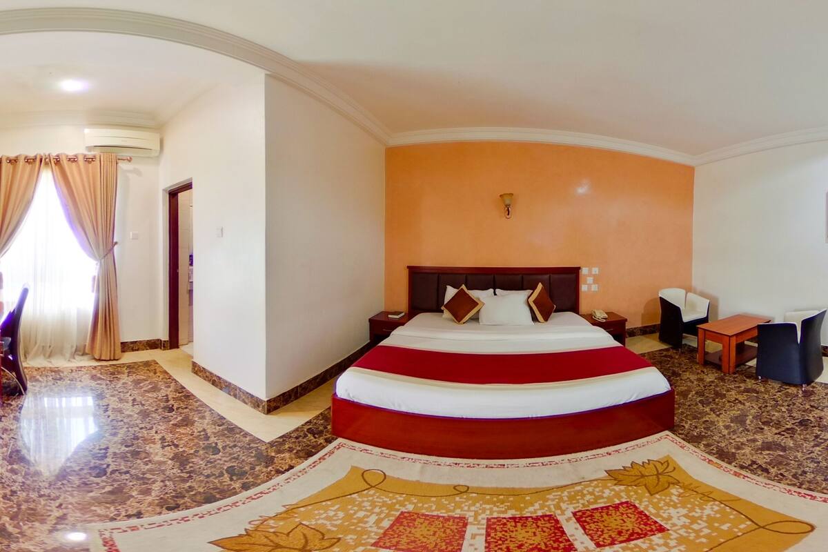 A hotel room with a large bed, a desk, a chair, a small table, and a TV.