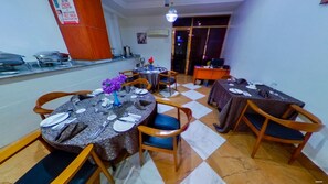 A dining area with round tables, chairs, and a checkered floor. There is a counter with glassware and a sign about phone and mask usage.