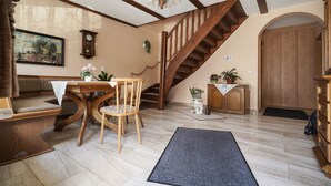 Una sala de estar acogedora con una escalera de madera, una mesa de comedor con sillas, una chimenea y una puerta grande de madera.