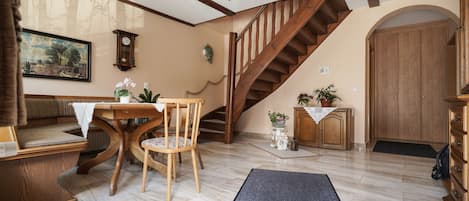 Una sala de estar acogedora con una escalera de madera, una mesa de comedor con sillas, una chimenea y una puerta grande de madera.