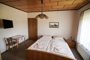 Un dormitorio con una cama de madera, un escritorio con una silla, un televisor en la pared y una ventana con cortinas.