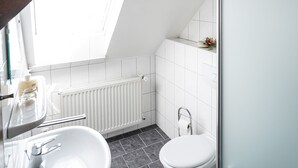 Un baño moderno con tragaluz, azulejos blancos, un lavamanos blanco y un inodoro.