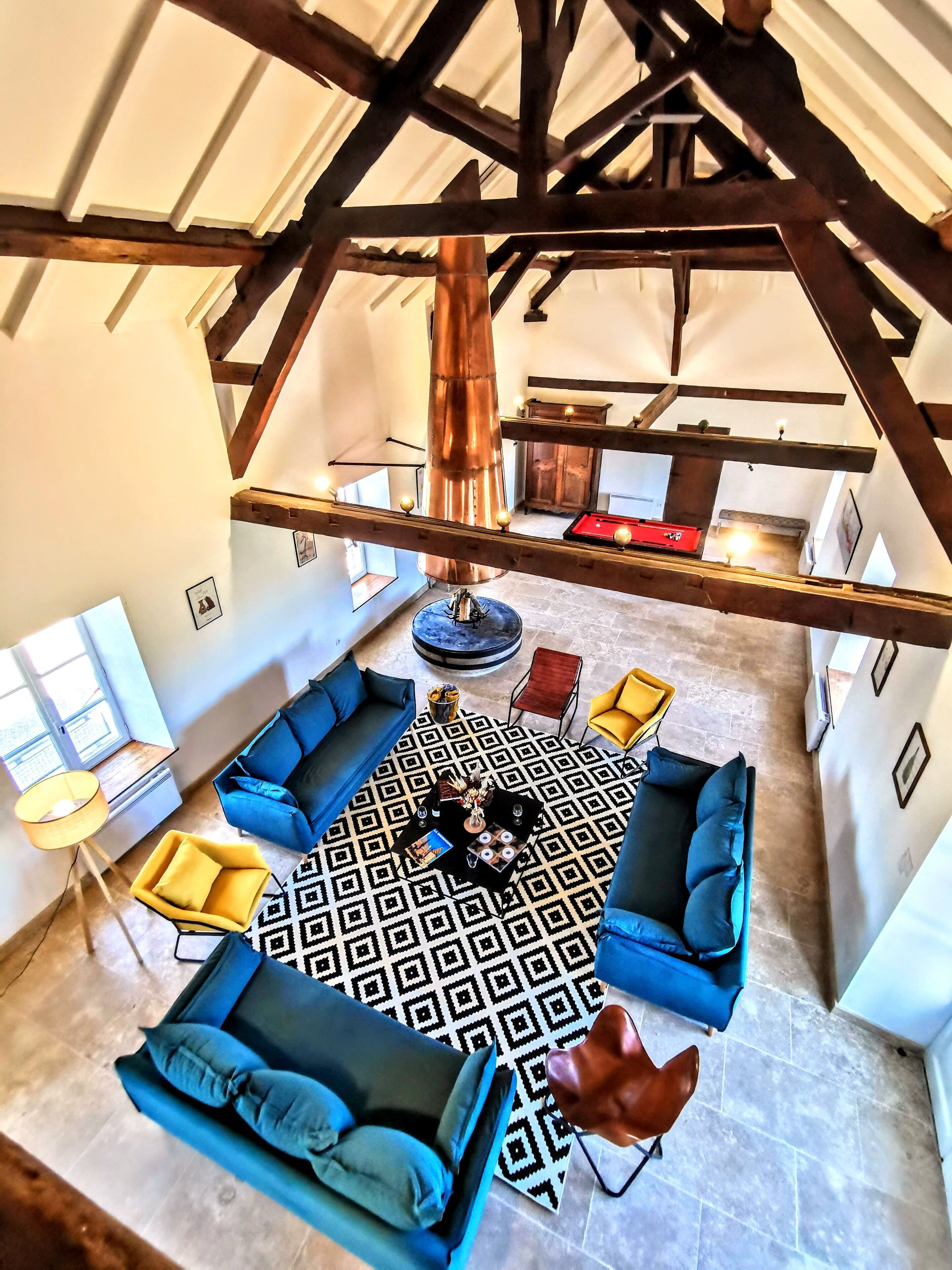 Een ruime loft met zichtbare houten balken, een vloer met patroon en een blauwe hoekbank.
