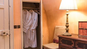 A room with a wooden dresser, a lamp, and a closet containing white robes. - Explore an entire castle whilst staying in historical splendour. (Peebles)