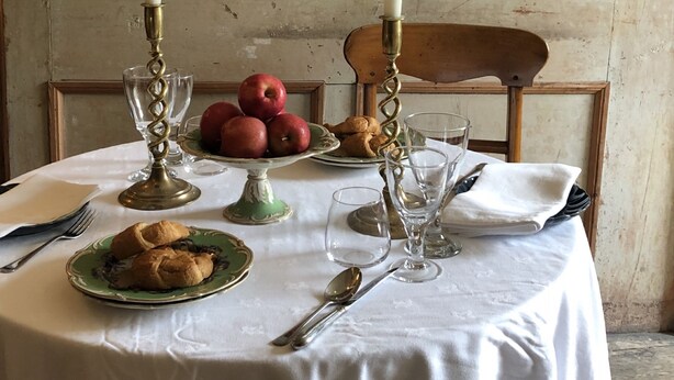 A table set with a white tablecloth, two lit candles, a plate of apples, a plate of croissants, and a green plate with a pastry. - Explore an entire castle whilst staying in historical splendour. (Peebles)