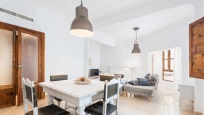 Ein Essbereich mit einem weißen Tisch und Stühlen, einem Fernseher und einer Couch im Hintergrund.