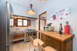 Une cuisine moderne avec des meubles en bois, un réfrigérateur en acier inoxydable, une cuisinière à gaz et un comptoir-bar en bois, agrémenté de tabourets de bar.