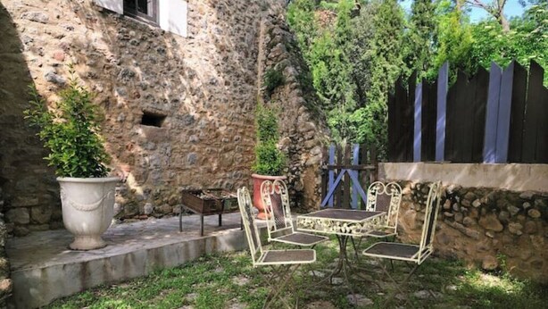 A stone wall, a metal table with chairs, and a potted plant in a courtyard. - Historical country house Costa Brava | Dali 2 Pax (Vilanant)