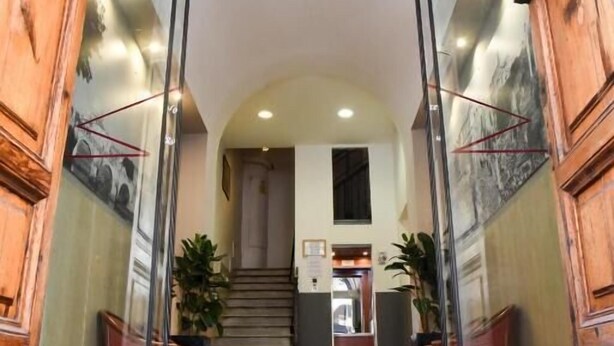Entrada de hotel con un cartel que dice "HOTELS" sobre una puerta de cristal, una escalera que da al interior y un mostrador de recepción visible a través del cristal.