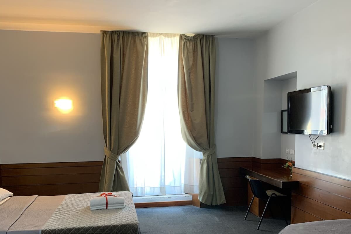 Una habitación de hotel con dos camas, un escritorio, un televisor y una ventana con cortinas.