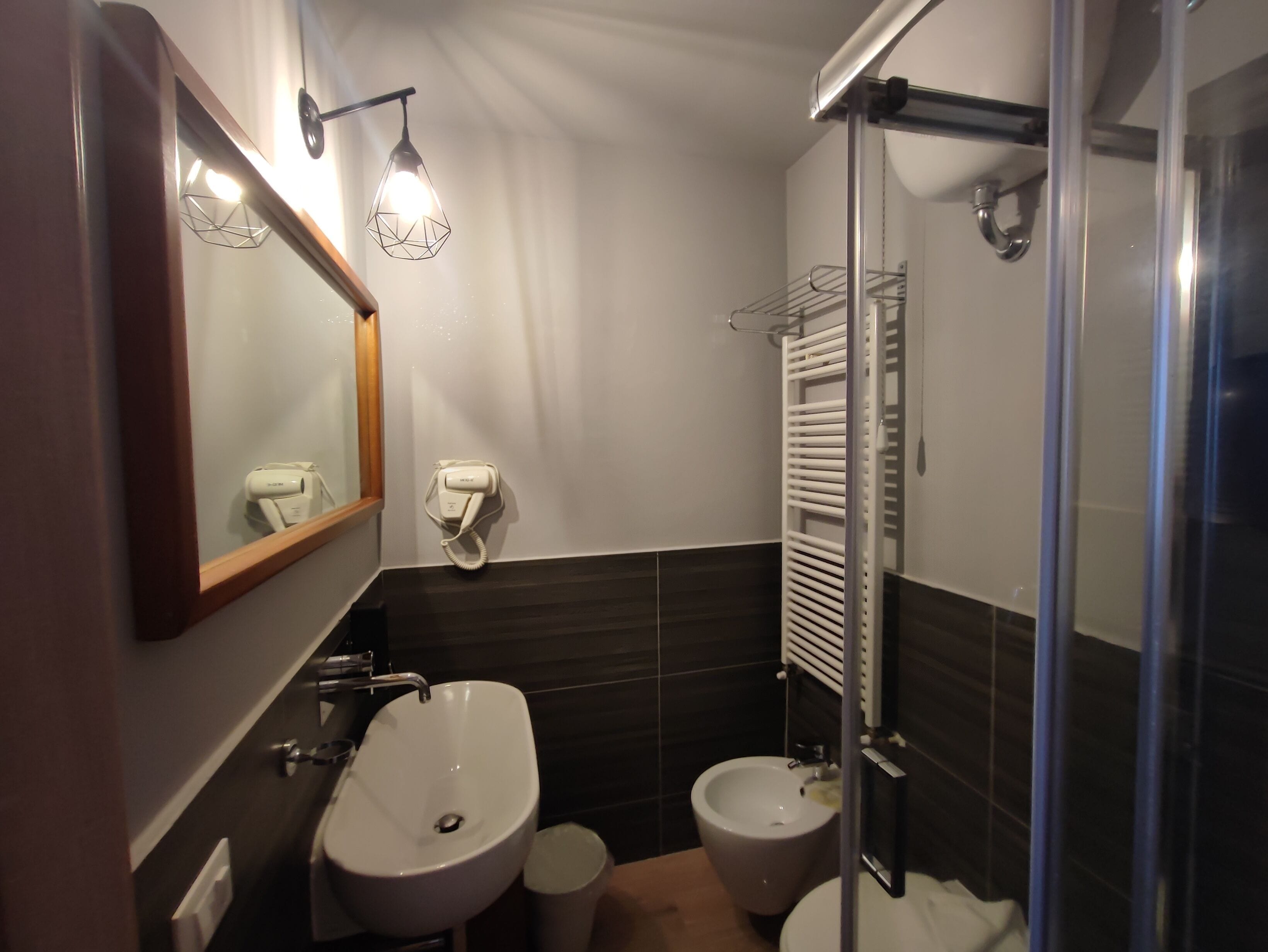 Een moderne badkamer met een wastafel, een bidet, een spiegel, een handdoekrek en een douchecabine met glazen wanden.