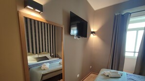 Una habitación de hotel con cama, televisión montada en la pared y una ventana con cortinas.