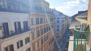 Una calle estrecha bordeada por edificios de varios pisos con balcones y una barandilla verde a la derecha.