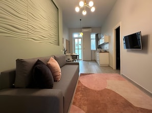 A modern living room with a sofa, a flat-screen TV, and a kitchen in the background. - Butik Art Hotel (Budapest)