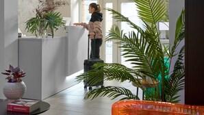 A lobby with a reception desk, a large window, and a plant. - Butik Art Hotel (Budapest)