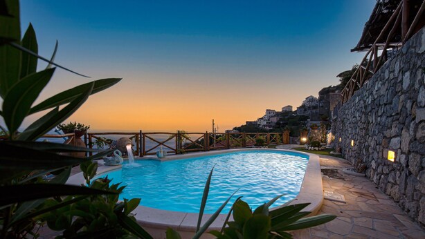 A swimming pool with a stone wall and a view of a coastal town at dusk. - Spring Villa with panoramic views and private pool (Furore)