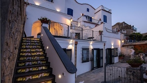 A multi-story building with a staircase decorated with flowers, balconies with railings, and outdoor lighting. - Spring Villa with panoramic views and private pool (Furore)