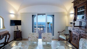 A room with a glass table, two floral chairs, a wooden cabinet, and a television on a stand. - Spring Villa with panoramic views and private pool (Furore)