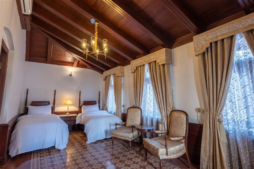 A hotel room with two beds, a chandelier, patterned carpet, and curtains.
