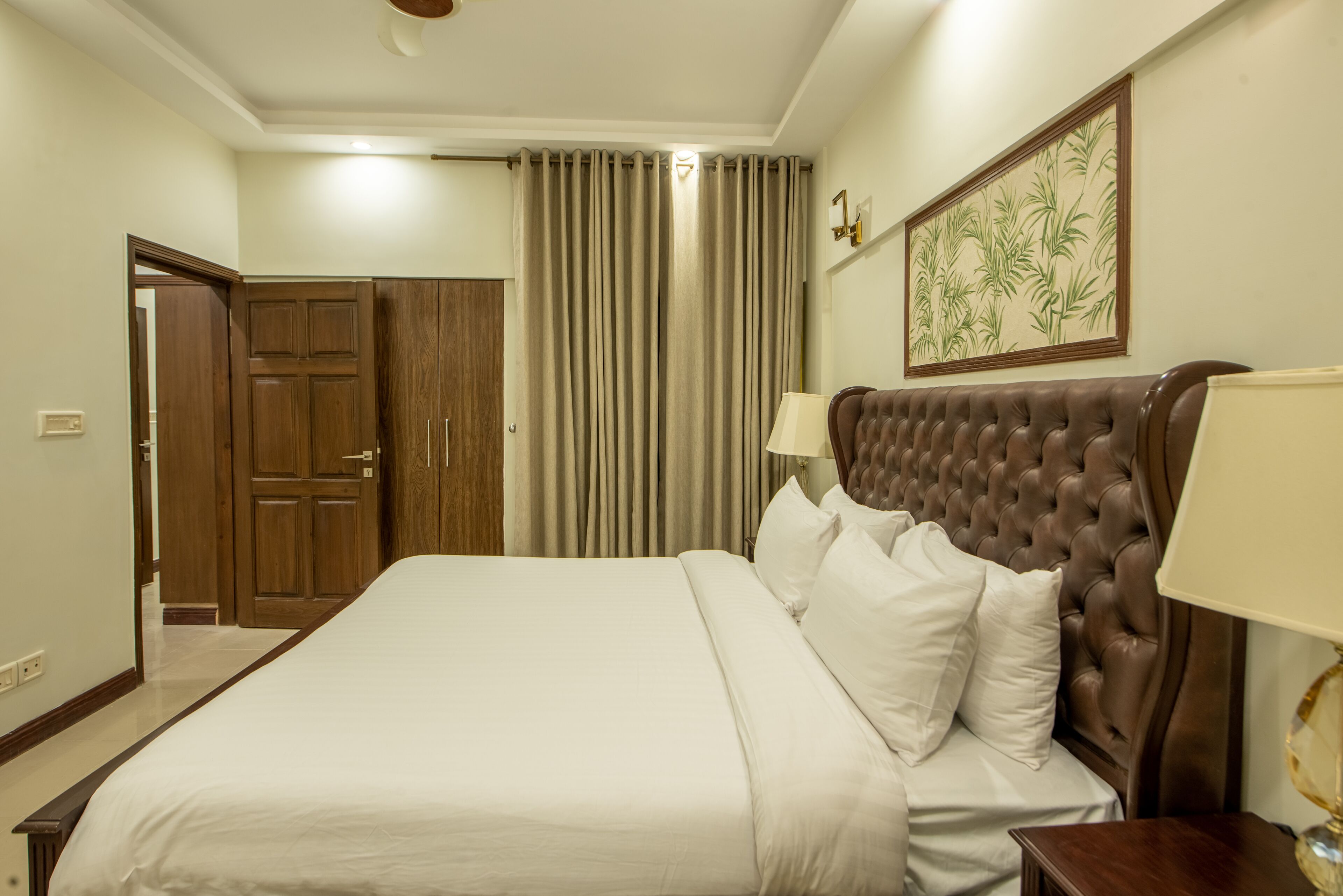 Cama bem arrumada com cabeceira estofada, porta de madeira e luminária fixada na parede.