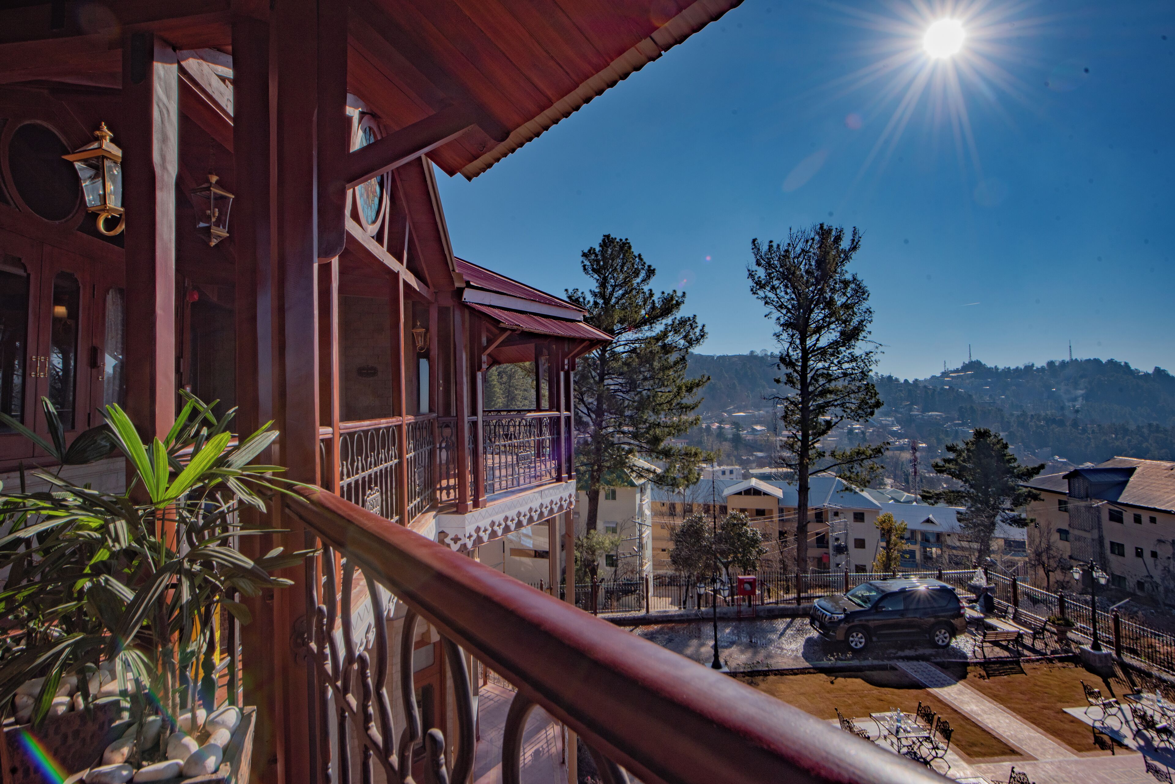 A balcony with a view of a town, a car parked on the street, and a clear sky.