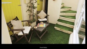 Un patio delantero con una mesa de madera, dos sillas, una planta en maceta y una escalera con césped artificial.