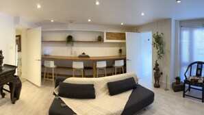 Una sala de estar con sofá, un comedor con sillas, una cocina y un cuadro grande en la pared.