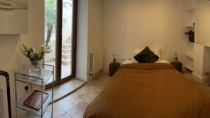 Un dormitorio con cama, mesita de noche, cómoda, radiador, ventana con vista a las escaleras y aire acondicionado de pared.