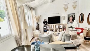 A modern living room with a sofa, a coffee table, and a TV. There is a bookshelf and a red chair. - House with spa surrounded by nature in Saint Paul de Vence (Saint-Paul-de-Vence)