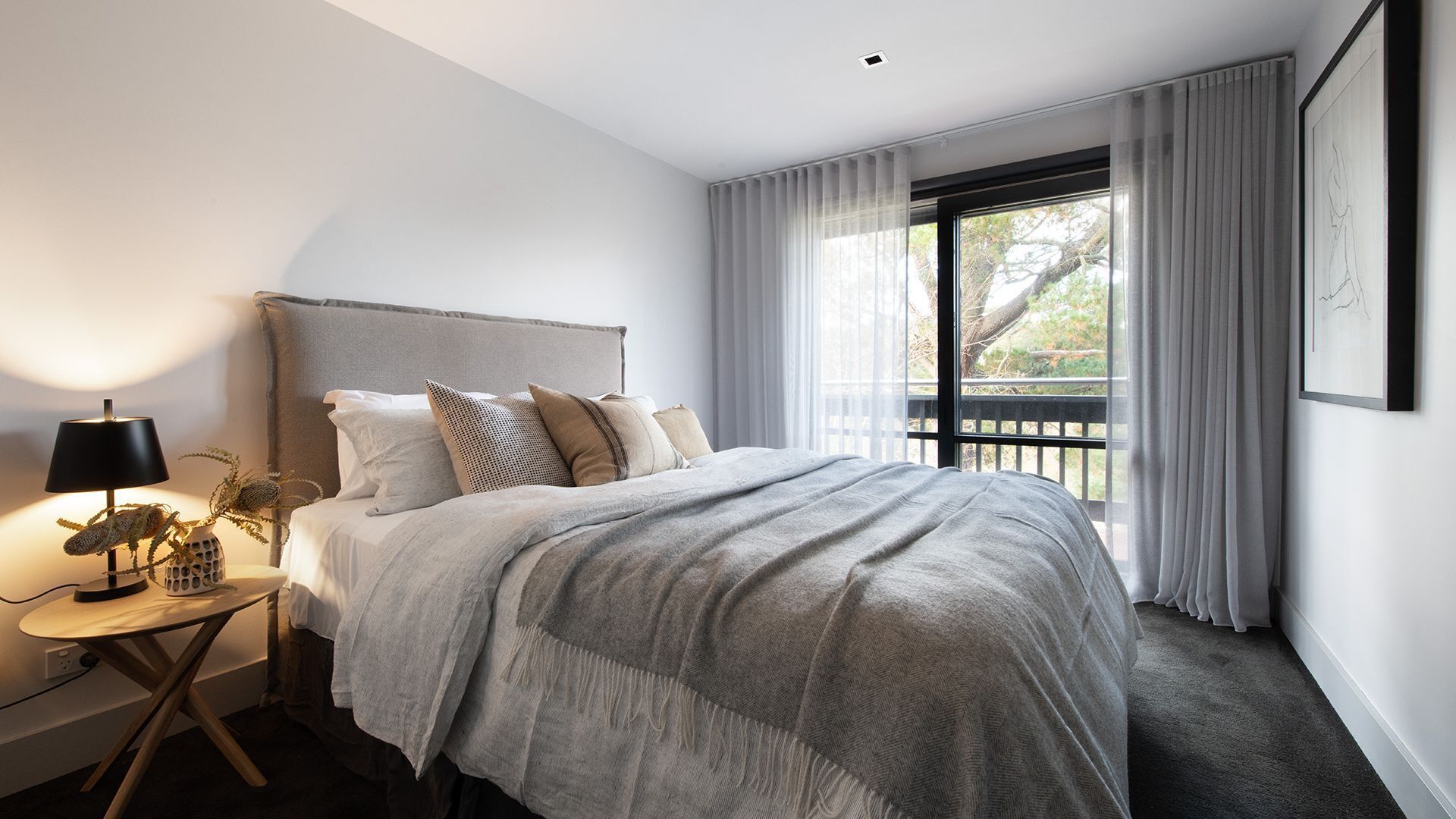 Un dormitorio moderno con una cama grande, una mesita de noche con lámpara y vistas al exterior a través de una ventana.