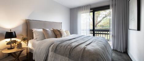 Un dormitorio moderno con una cama grande, una mesita de noche con lámpara y vistas al exterior a través de una ventana.