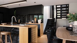 A modern kitchen with black cabinetry, a wooden island, and a dining area with black chairs. - Mi Casa Su Casa - stylish Interiors with Sauna! (Hepburn Springs)