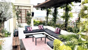 Une terrasse sur le toit avec un canapé d’angle, une petite table et un banc en bois. On y trouve également des plantes en pot et une pergola.