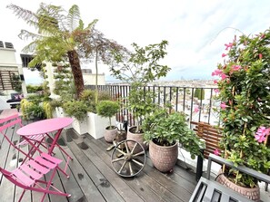 Un balcon agrémenté de plantes en pot, une chaise rose et une table en bois.