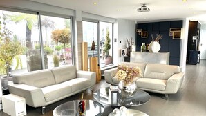Un salon moderne avec un canapé beige, une table basse agrémentée d’objets décoratifs et de grandes fenêtres donnant sur l’extérieur.