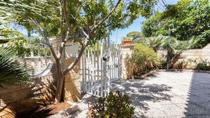 A gated entrance with a gravel driveway, surrounded by various plants and trees. - Villetta Anna Torre Suda (Racale)