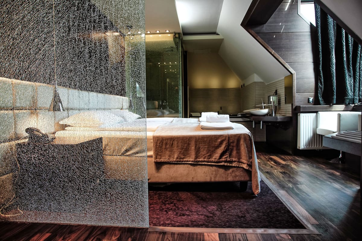 A modern hotel room with a large bed, a sitting area with a sofa and a coffee table, a bathroom with a bathtub and a sink, and a view of the city through large windows.