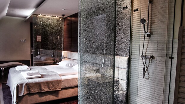 Una habitación de hotel moderna con una cama grande, un separador de vidrio y una zona de ducha.