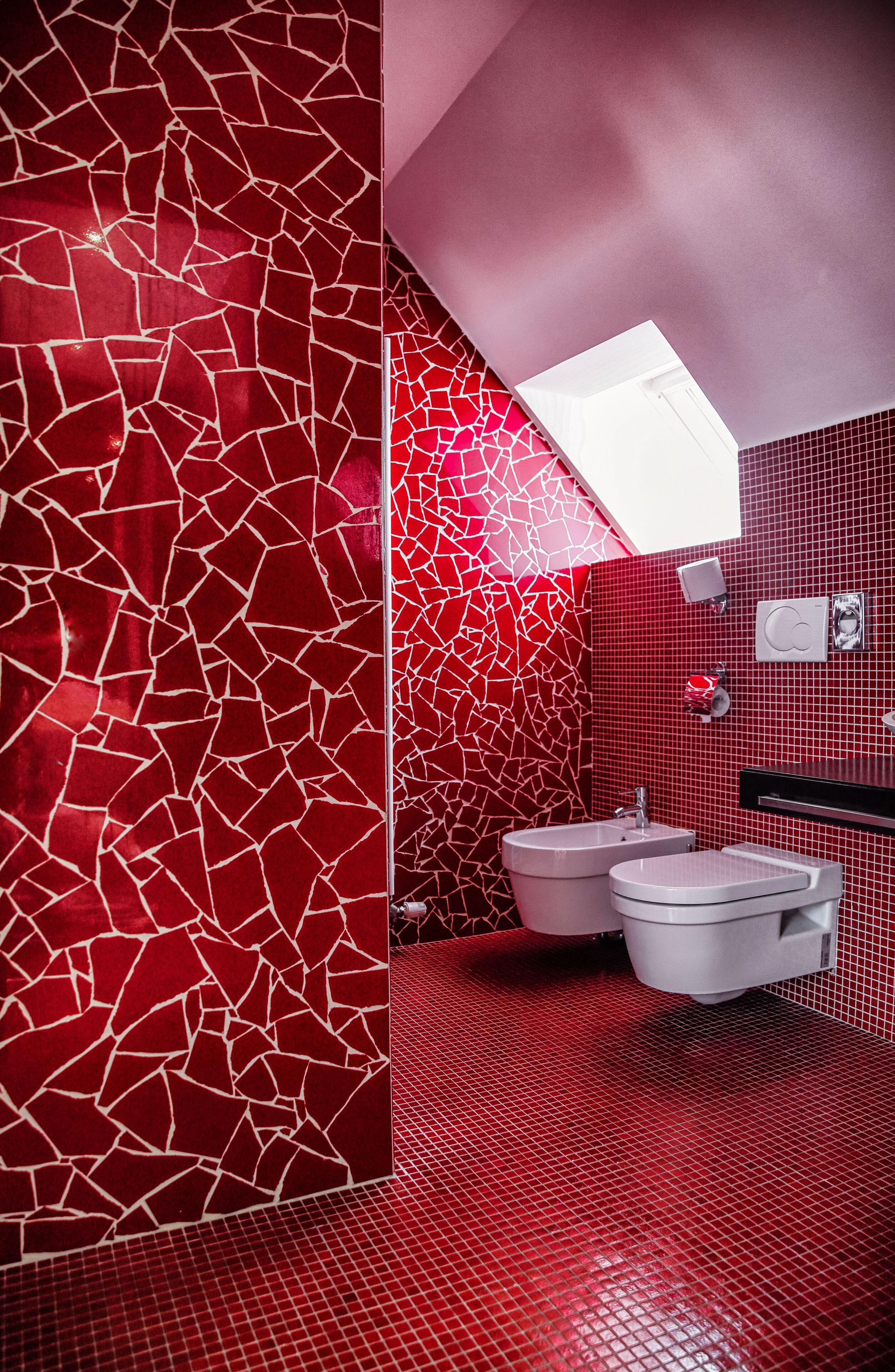 A modern bathroom with red mosaic walls and a white sink.