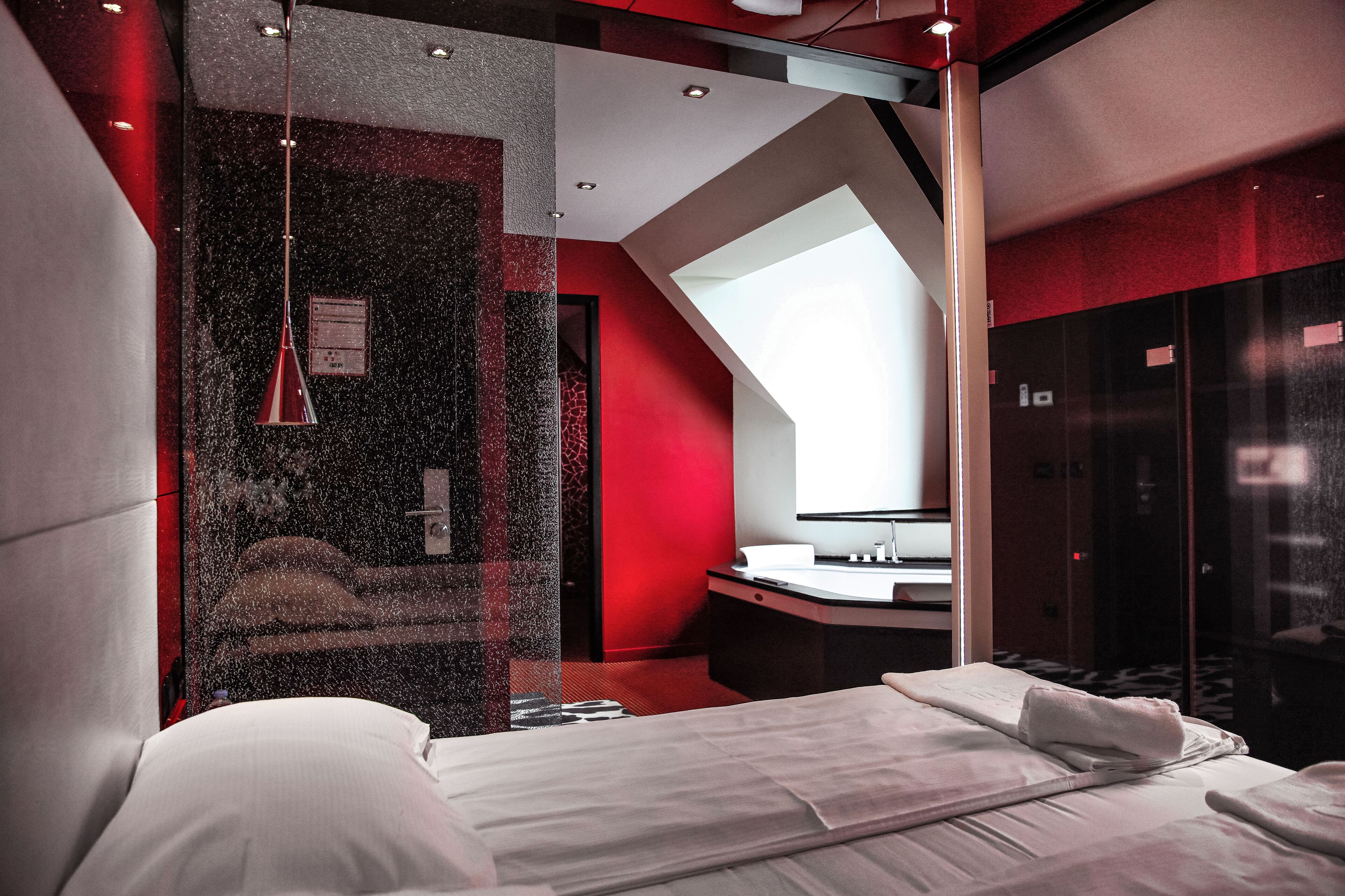 A modern hotel room with a bed, a bathroom with a mirror, and a red accent wall.