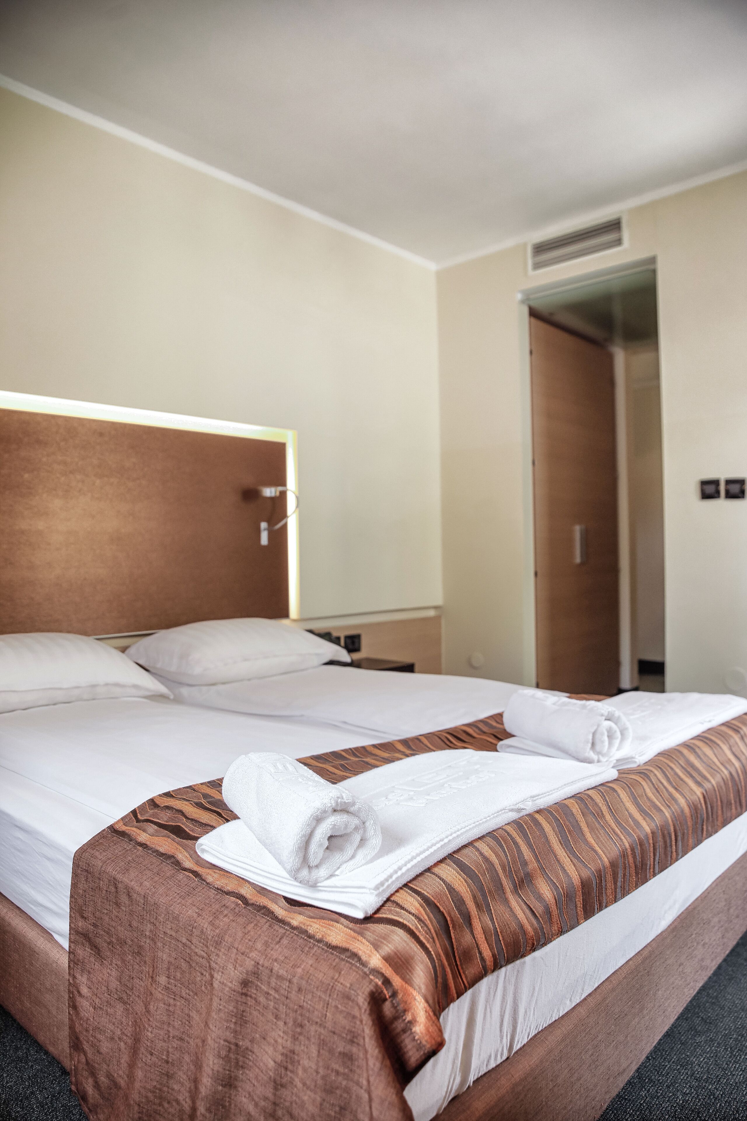 A hotel room with a large bed, a wooden headboard, a nightstand, and a mirror.