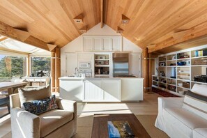 Amplia sala de estar con techo de madera, una isla central en la cocina y una estantería.