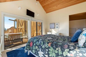 Quarto com cama grande, TV fixada na parede e porta de vidro deslizante para área externa.