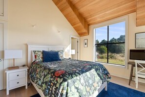 Ein Schlafzimmer mit einem Bett, einem Nachttisch, einem Schreibtisch und einem großen Fenster.