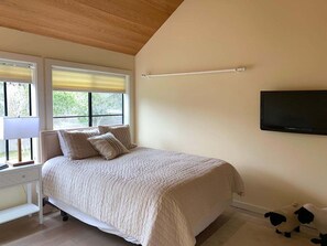 A bedroom with a bed, bedside table, lamp, and a television on the wall. - Charlie's Retreat | Hot Tub & EV Charger (Sea Ranch)